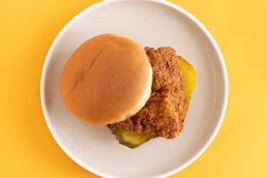 The fried chicken sandwich on a white plate on a yellow background.