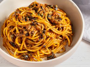 Pasta puttanesca, made with spaghetti, in a white bowl.