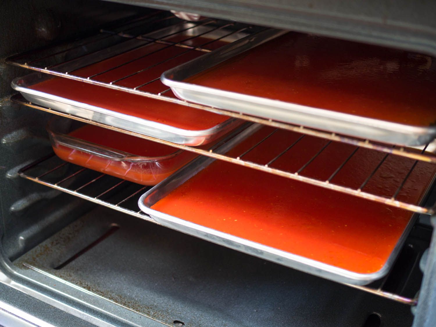 在烤箱的架子上放几个带边的烤盘和平底锅，里面装满了番茄水。