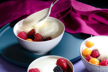 Zabaglione being spooned into a bowl of fruit with two other topped bowls in the foreground