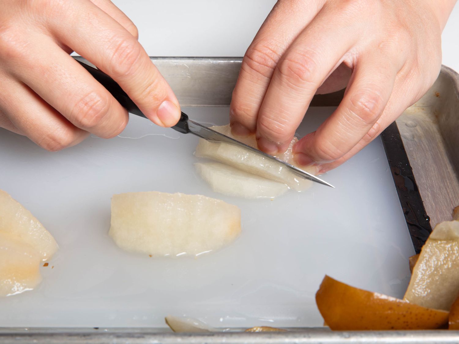 解冻冻梨切片在一套切肉板边的烤盘