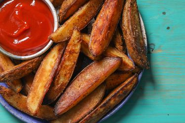 Closeup of a serving plate of roasted potato wedges with a ramekin of ketchup.
