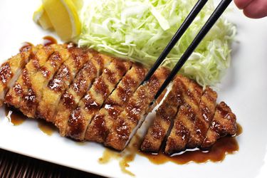 sliced chicken katsu drizzled with sauce, plated with lemon wedges and shredded cabbage.