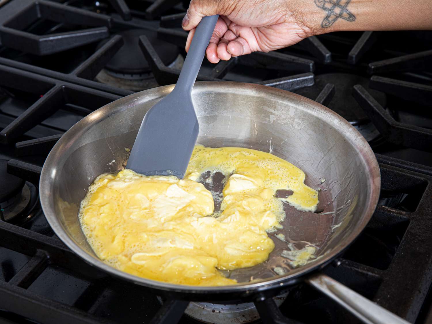 一只手拿着灰色的硅胶锅铲，在不锈钢煎锅里炒鸡蛋