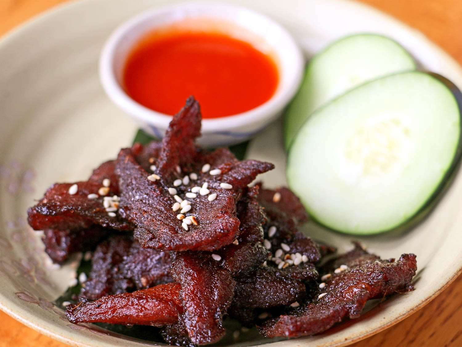 一盘深红色的晒干猪肉(muu haeng)，旁边是黄瓜片和一小碗蘸酱