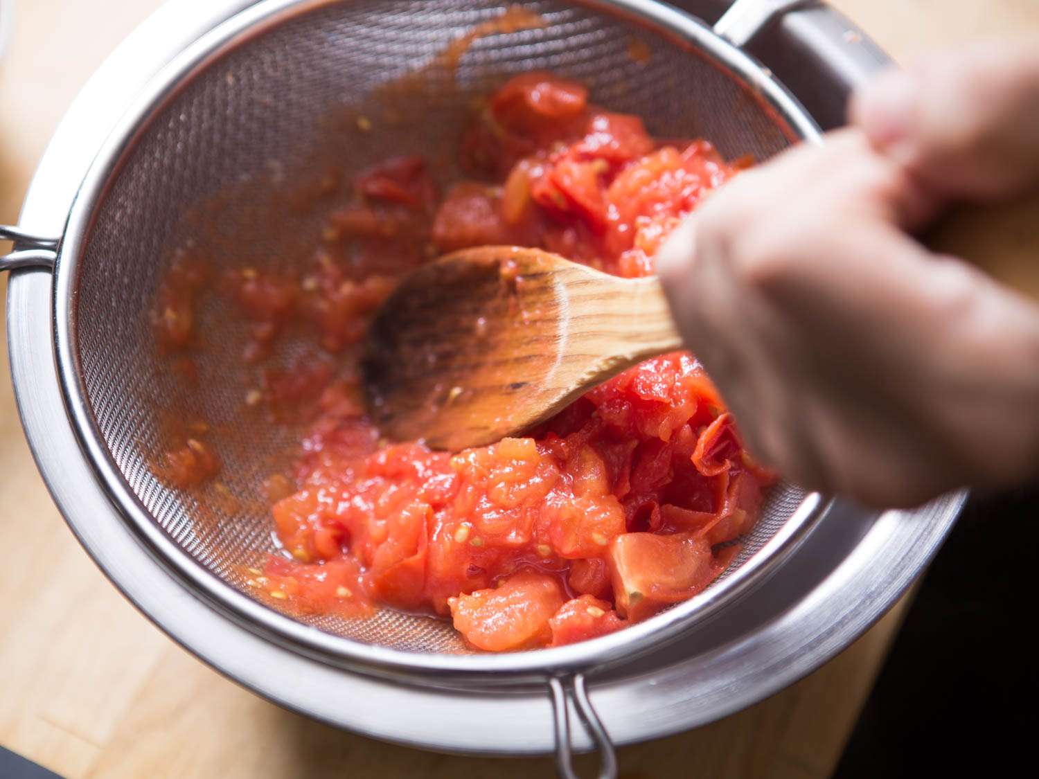 用木勺将西红柿压过细网滤网