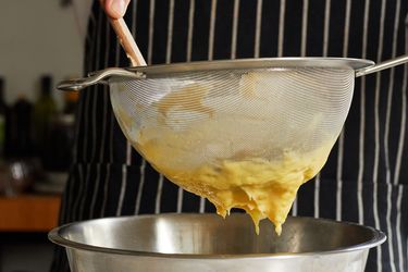 Pastry cream being strained through a fine mesh strainer into a stainless steel bowl