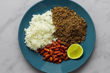 SalpicÃ³，白米饭，红芸豆，一片青柠放在大理石柜台的蓝色盘子上。
