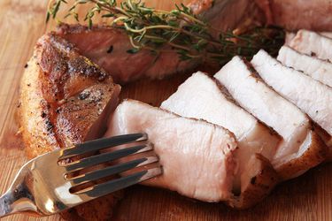 在砧板上切好的带骨头的熟猪排。叉子是一片。猪肉片旁边有一根新鲜的百里香。