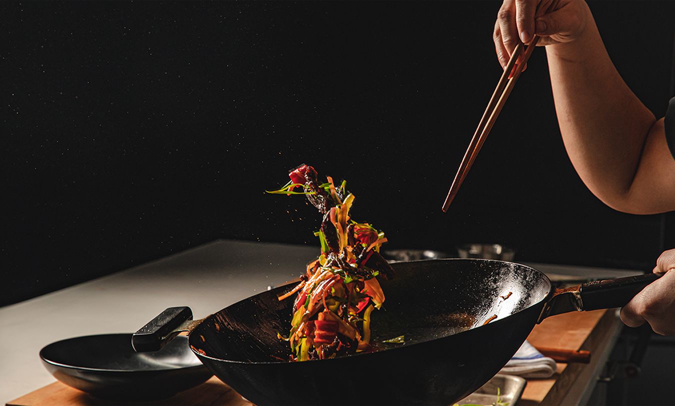 在黑暗的厨房里，一个人拿着筷子翻炒锅，导致五彩缤纷的食物悬浮在空气中