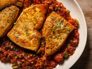Deeply browned braised swordfish steaks on a platter with a rich tomato, caper, olive sauce.