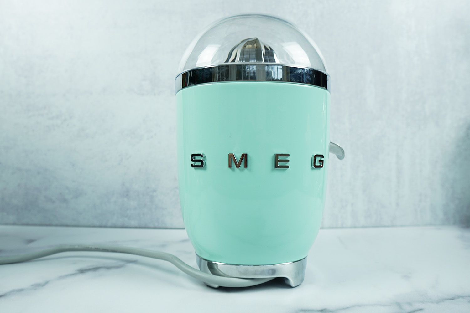 a light green Smeg electric citrus juicer on a marble surface