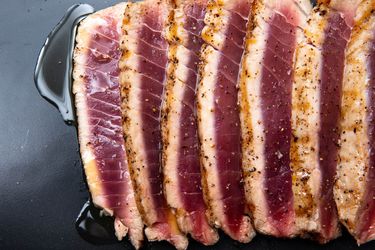 Sliced grilled tuna, cooked rare, on a black plate, seasoned with salt and freshly ground black pepper and drizzled with olive oil.