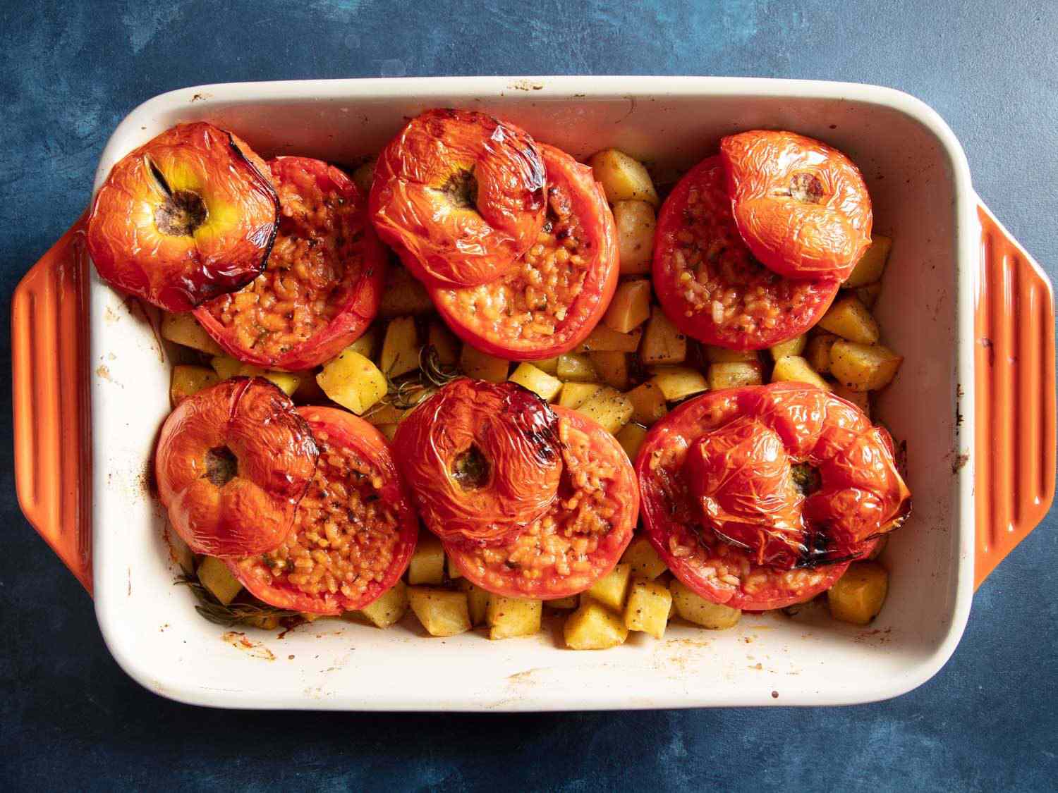 Overhead of baking dish with finished rice-stuffed tomatoes and roast potatoes.
