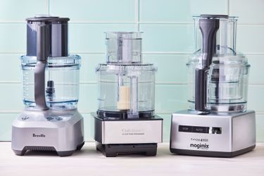 Three food processors against a blue tile background