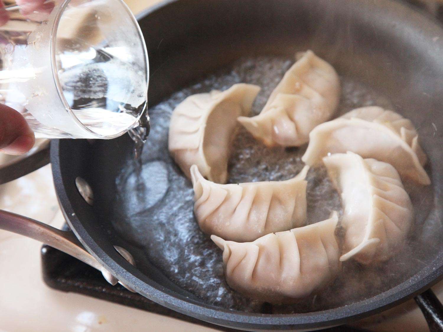 往装有六个日式饺子的不粘锅里加水。