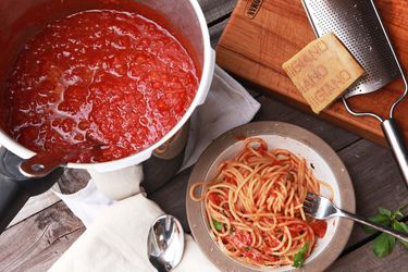 Overhead shot of a pot of pressure cooker tomato sauce, bowl of pasta tossed in tomato sauce, and hunk of parmigiano resting on a cheese grater