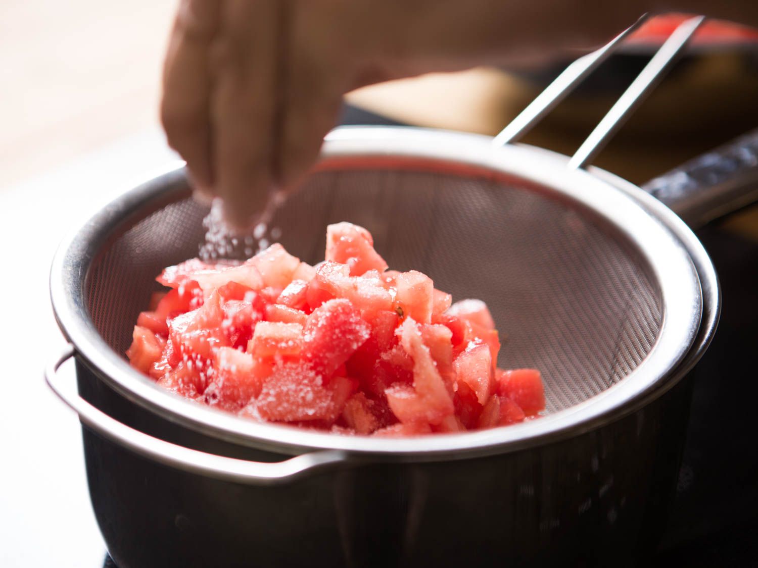 在筛子里用盐腌西红柿丁。