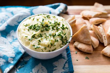 Bowl of puree potato topped with fresh herbs next to a pile of sliced pita bread