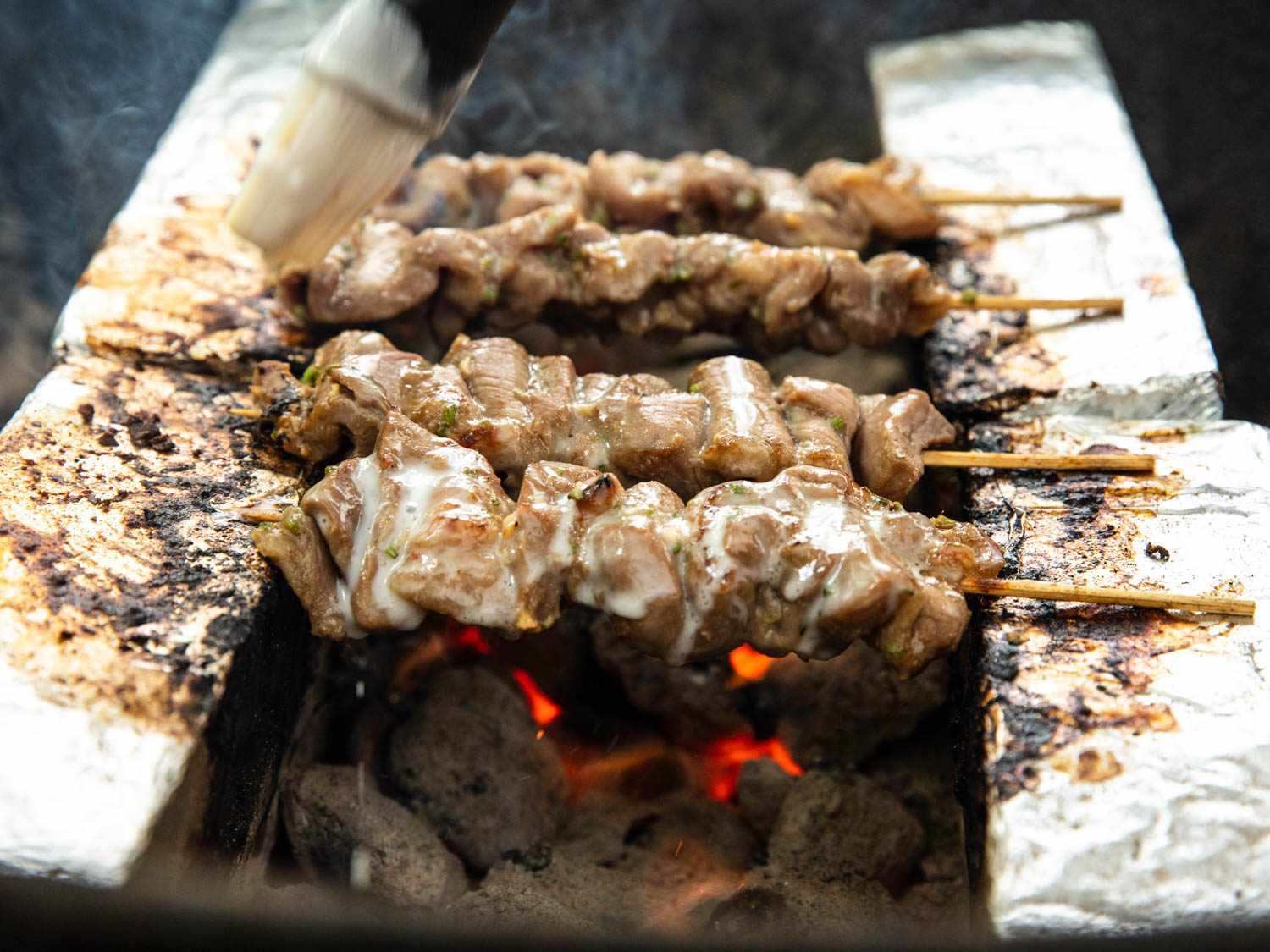几根泰式猪肉串在木炭上烤着，悬挂在两排平行的锡纸包裹的砖块之间