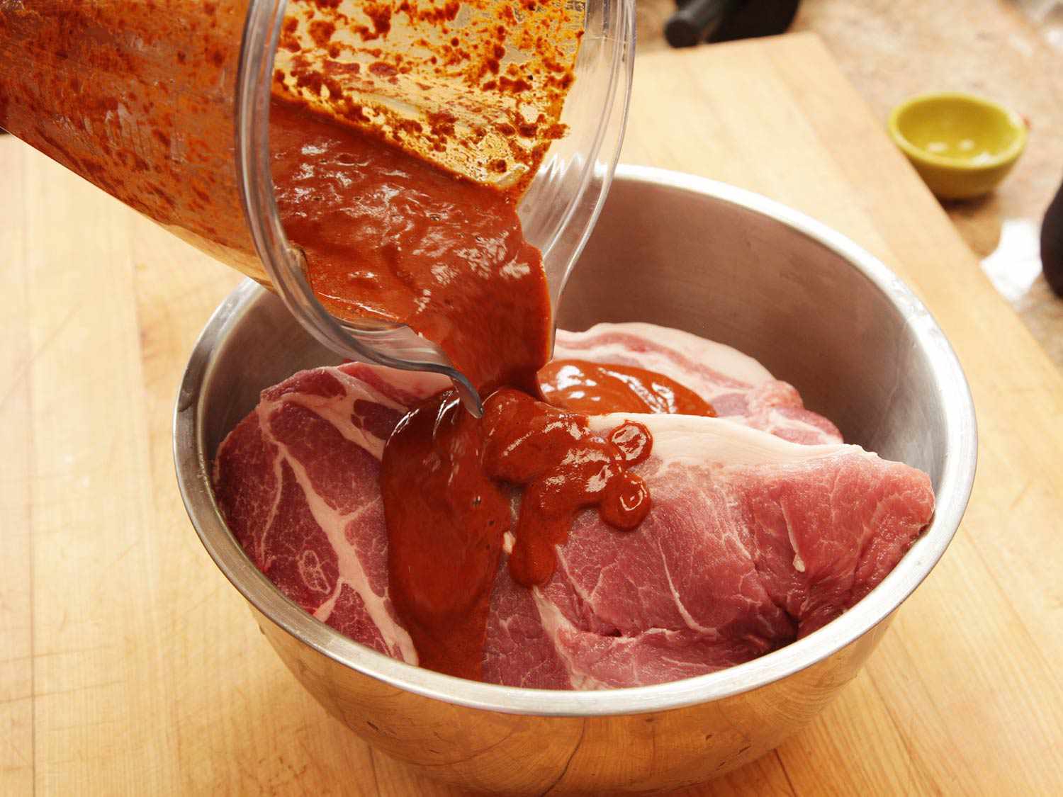Pouring sauce on the raw pork for cochinita pibil recipe.