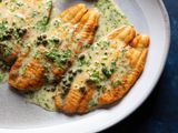 Deep golden brown fish fillets on a large serving platter are covered in a creamy, glossy, perfectly emulsified butter sauce, studded with capers and flecked with minced parsley.