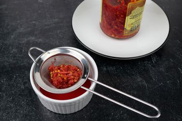 a small fine mesh strainer drains hot peppers of their oil