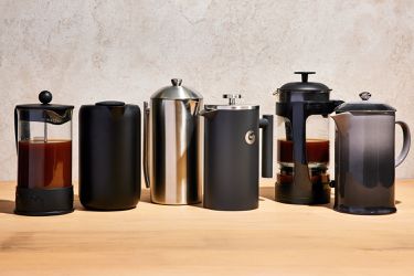 Six coffee makers on a wooden surface against grey background