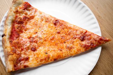 一块纽约风格的奶酪披萨放在一个白纸盘子上。