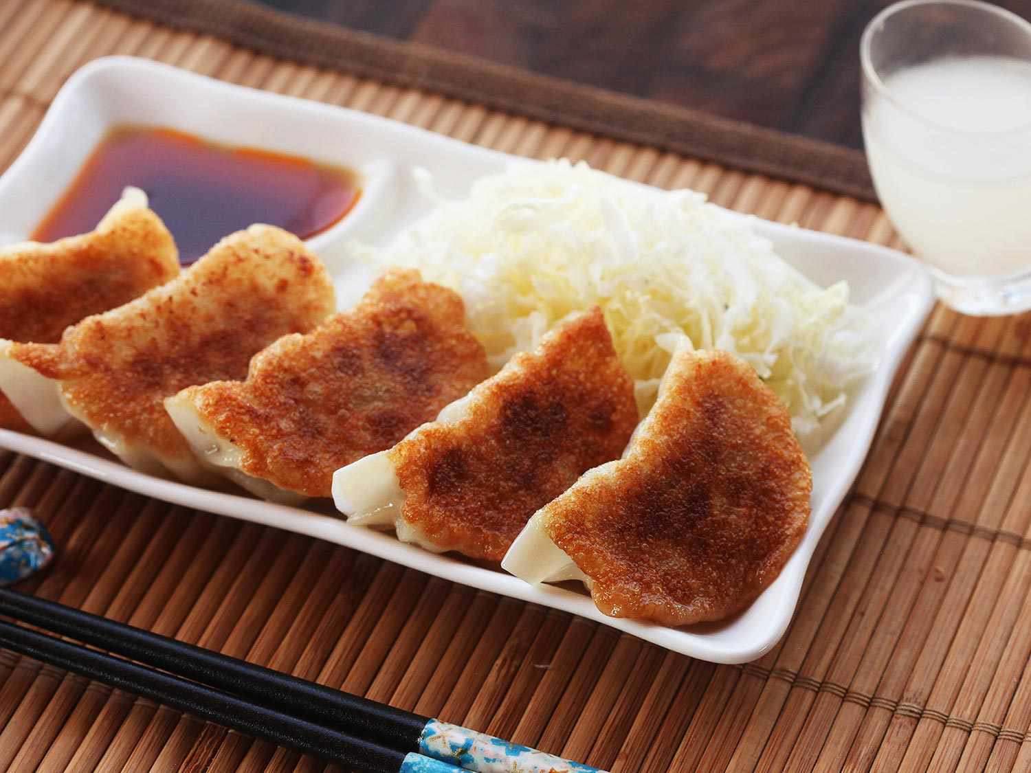五个日式煎饺放在一个小白盘子里，蘸酱和卷心菜。所有饺子的酥面都朝上。