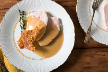 Sliced sous vide turkey breast with crisp skin cracklings and gravy on a white plate.
