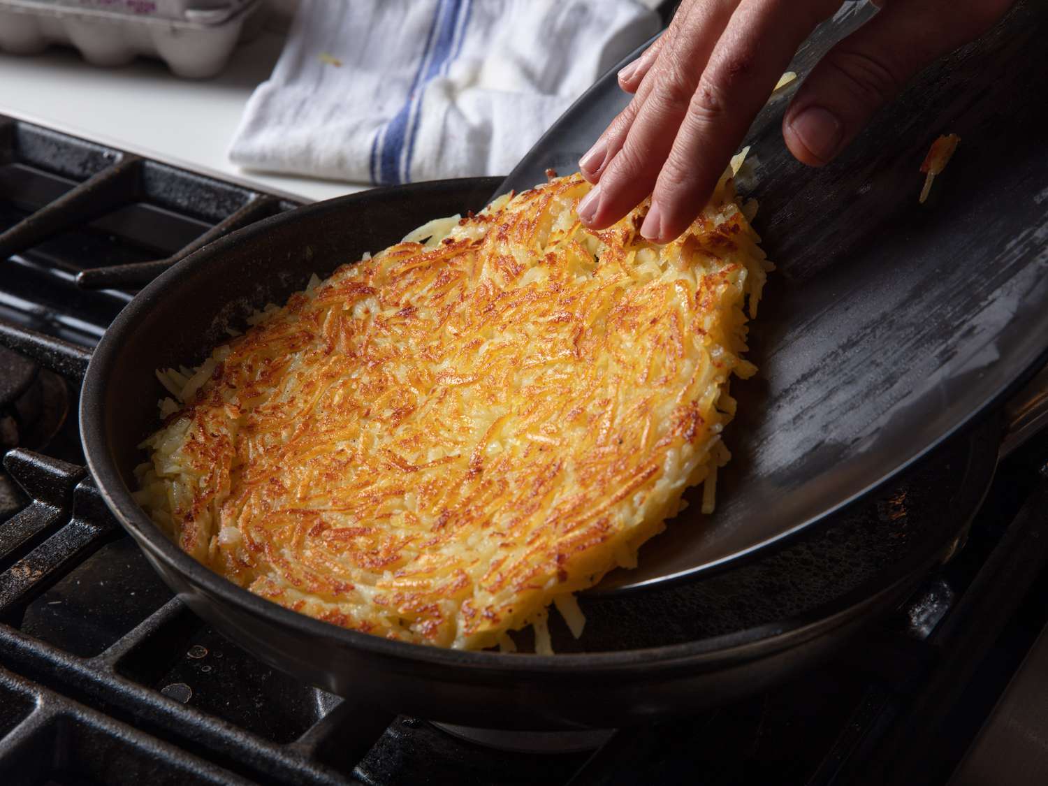 Sliding the flipped rÃ¶sti from a plate back into the skillet to brown the second side.