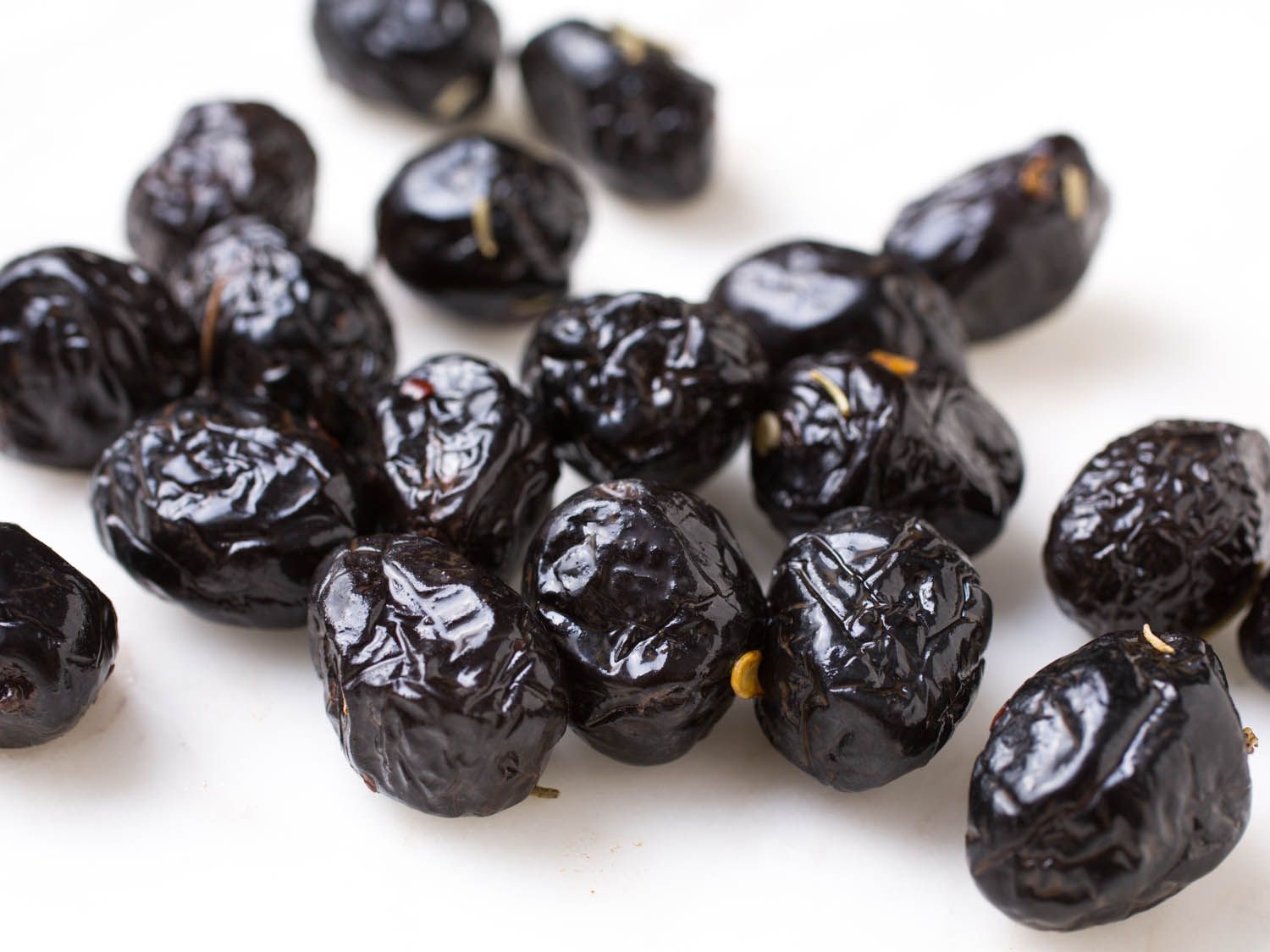 有光泽的，非常皱的黑橄榄覆盖在白色表面的辣椒片特写