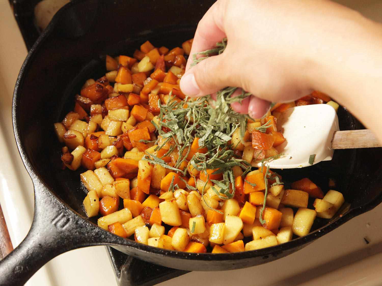 将切碎的鼠尾草撒在盛有炒好的南瓜块和苹果块的平底锅上。