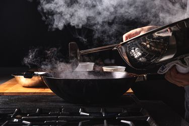A lid being removed off a smoking wok