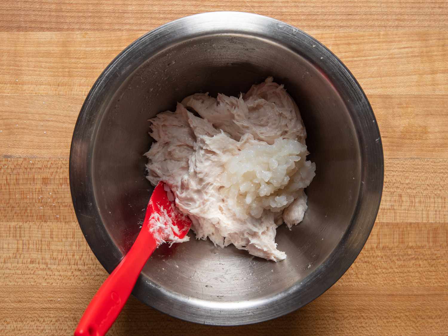 用红色抹刀将加工过的鱿鱼混合物和切碎的鱿鱼放在碗里
