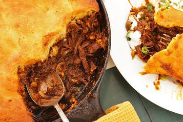 Plate with a portion of tamale pie next to the pie in a cast iron skillet