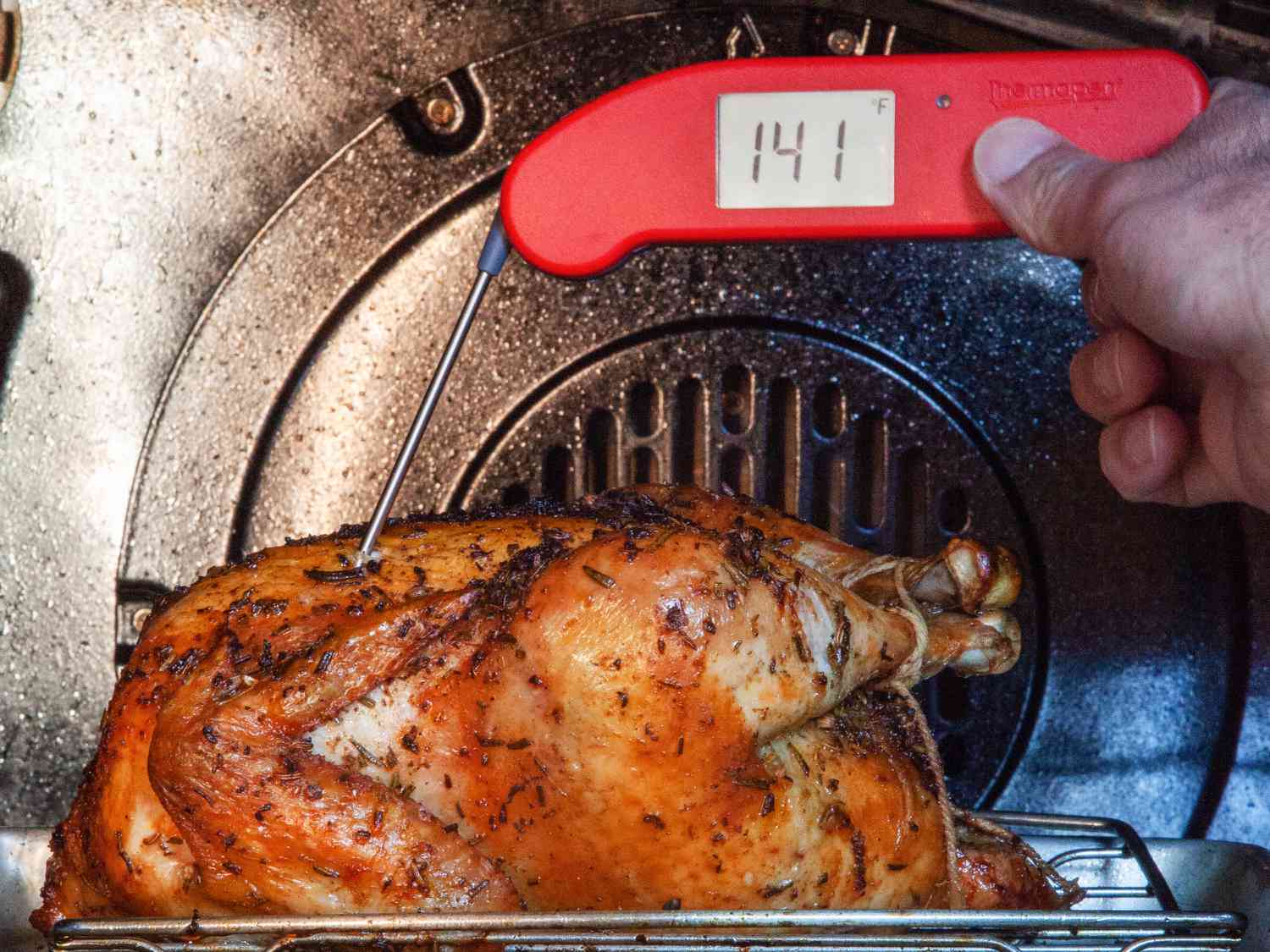 a person using an instant-read thermometer to take the temperature of a chicken roasting in the oven