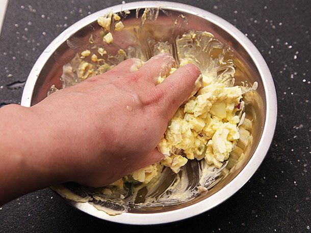 作者的手伸进一碗煮熟的鸡蛋，将它们挤压成奶油状的块状。