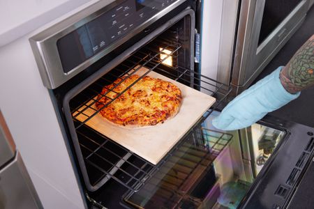 拿一个微波炉手套拉石头烤披萨从烤箱里拿出来