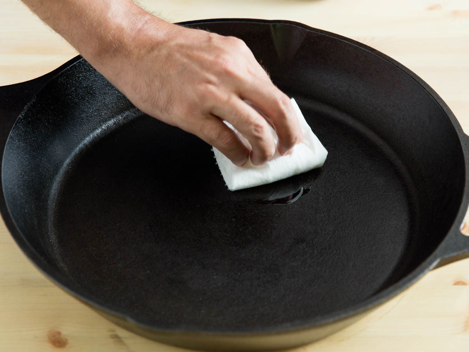 A hand wiping holding a paper towel and wiping the interior of a cast iron skillet with oil