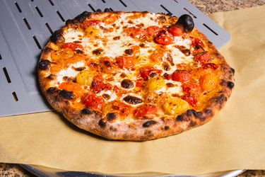 爆裂的樱桃番茄户外烤箱披萨，从皮上滑到披萨盘上的羊皮纸上