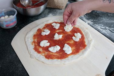 一只手在比萨饼浇头mozerella木制披萨皮