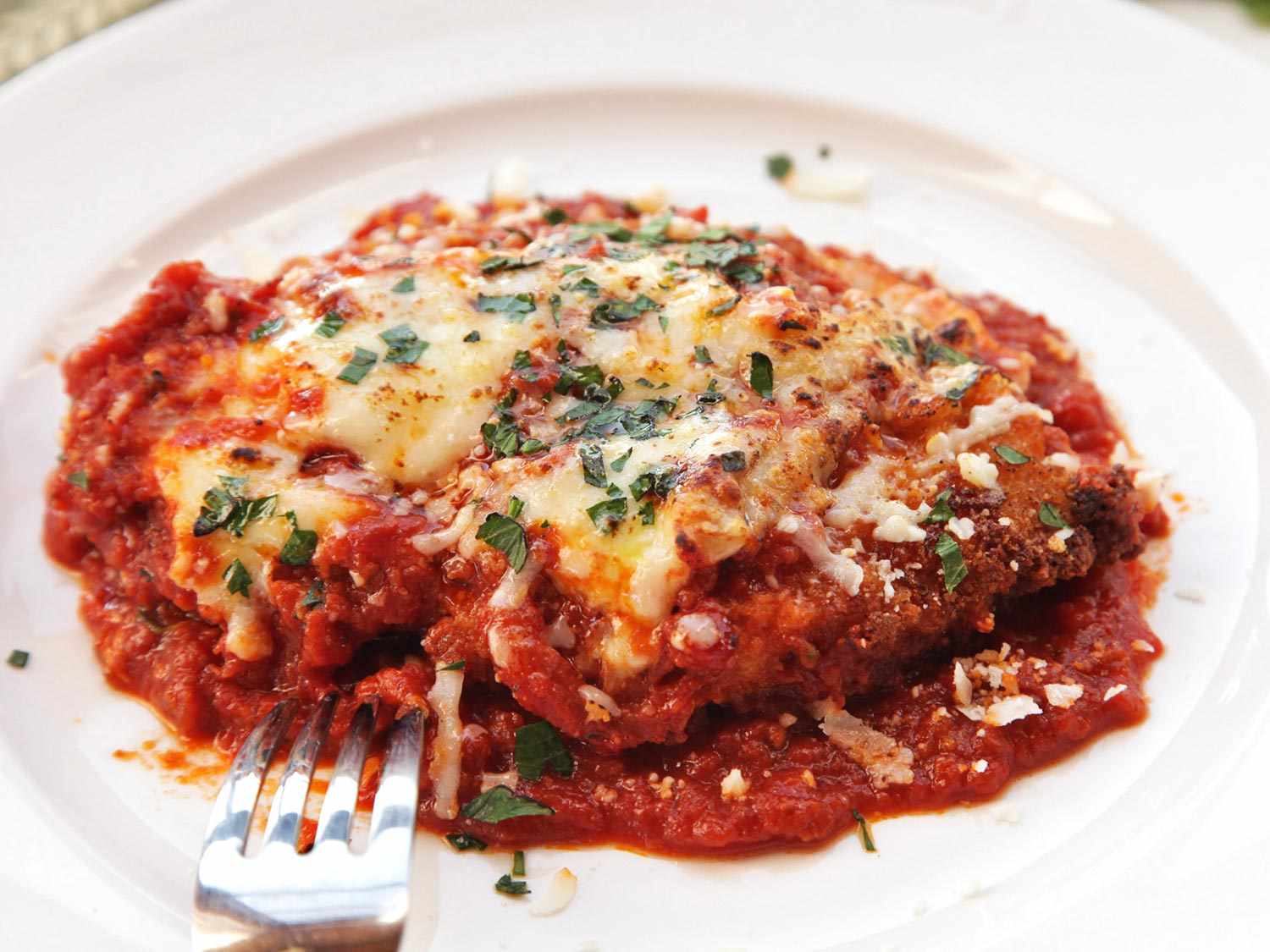 Taking a fork to a plate of chicken parmesan