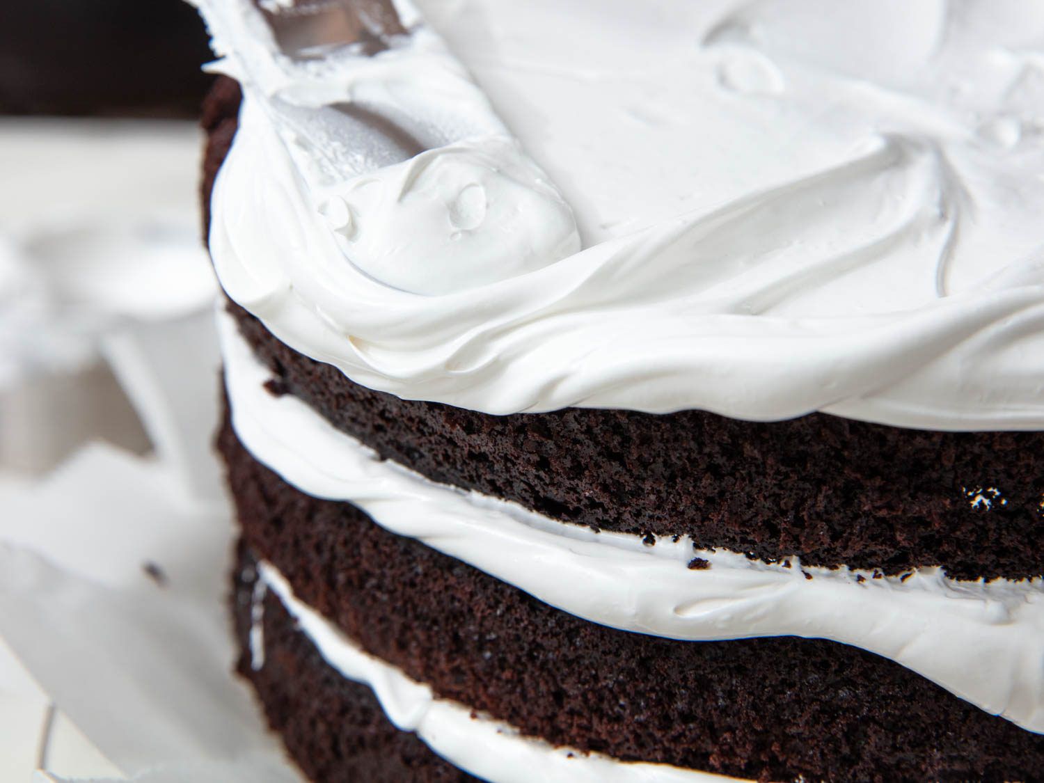 用抹刀在三层巧克力蛋糕上涂上7分钟的蓬松糖霜，蛋糕的黑色一面仍然暴露在外
