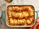 Browned hasselback potatoes in a blue stoneware baking dish on a linen tablecloth.