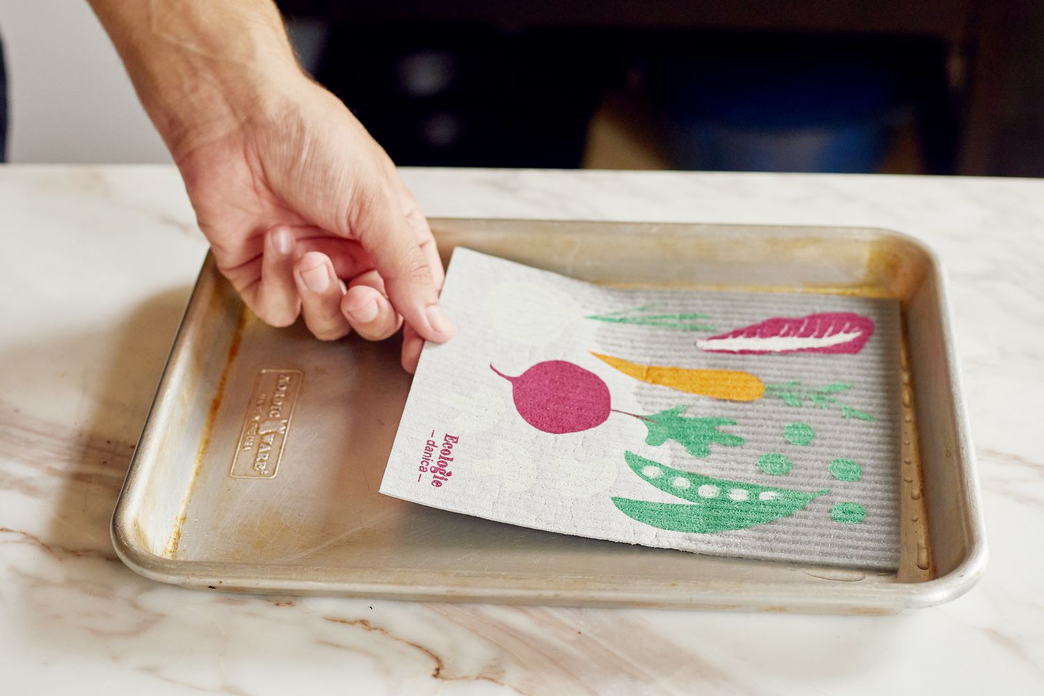 a person placing a swedish dishcloth into a quarter sheet pan filled with water