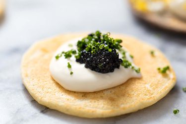 A blini topped with creme fraiche, caviar, and chives.