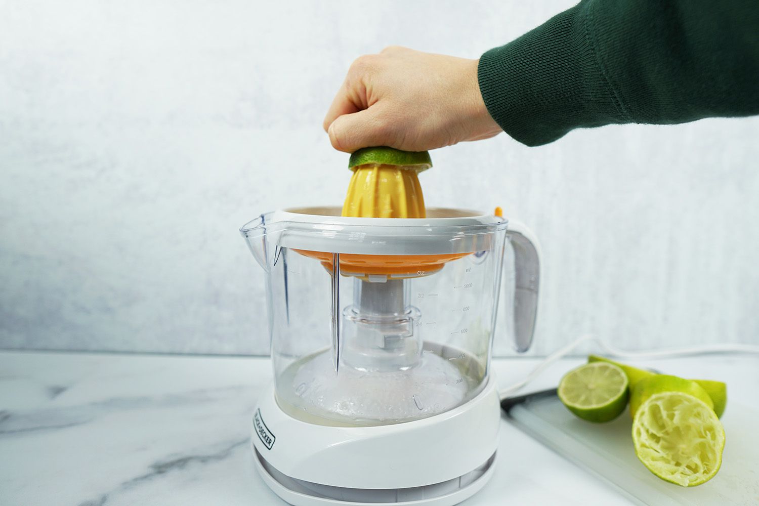 A hand juicing a lime half on an electric citrus juicer