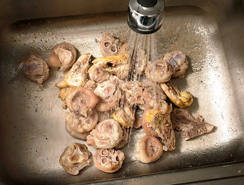 在一个大的不锈钢水槽里清洗焯过水的猪肉和鸡骨。